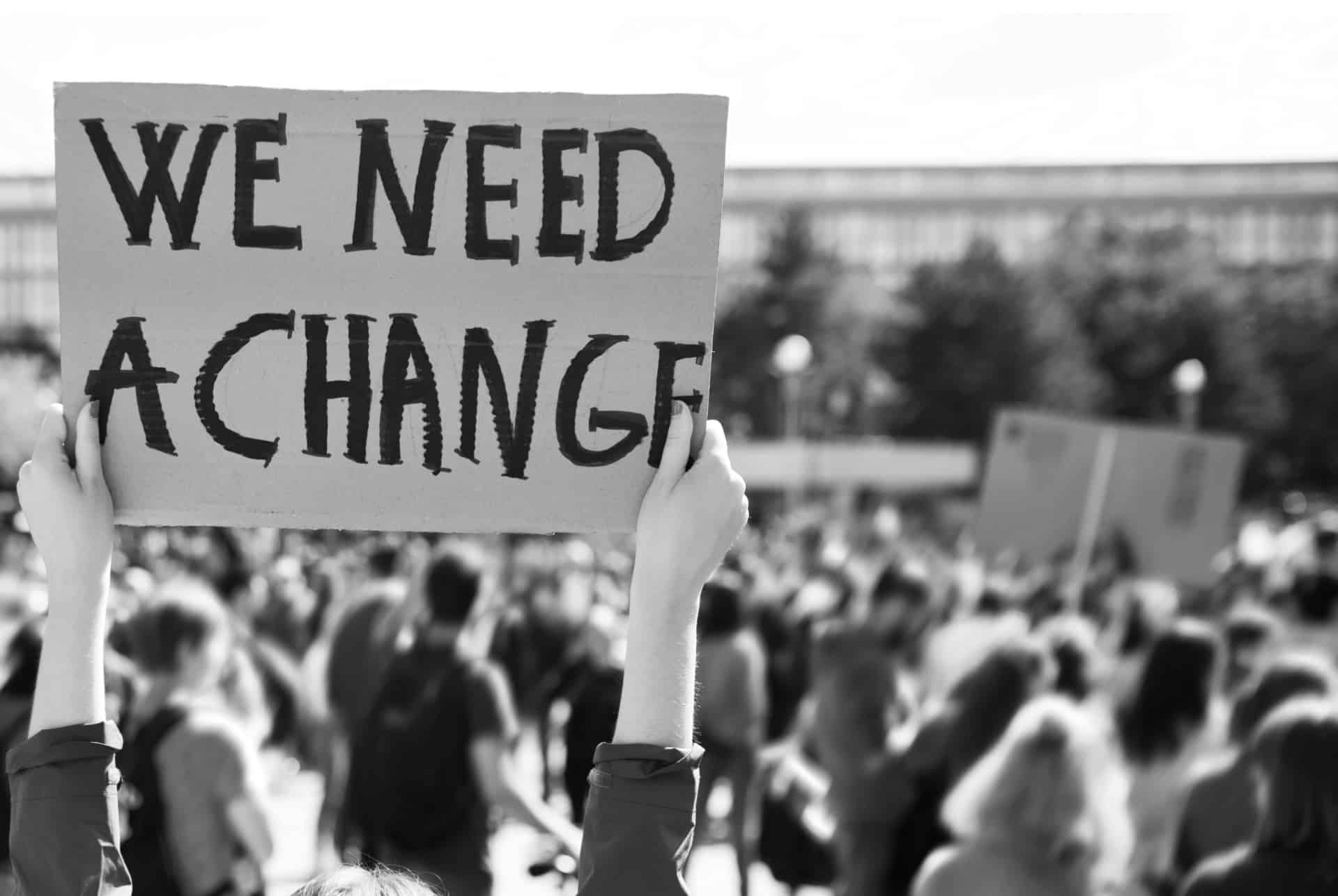 A person holding up a sign that says we need a change.